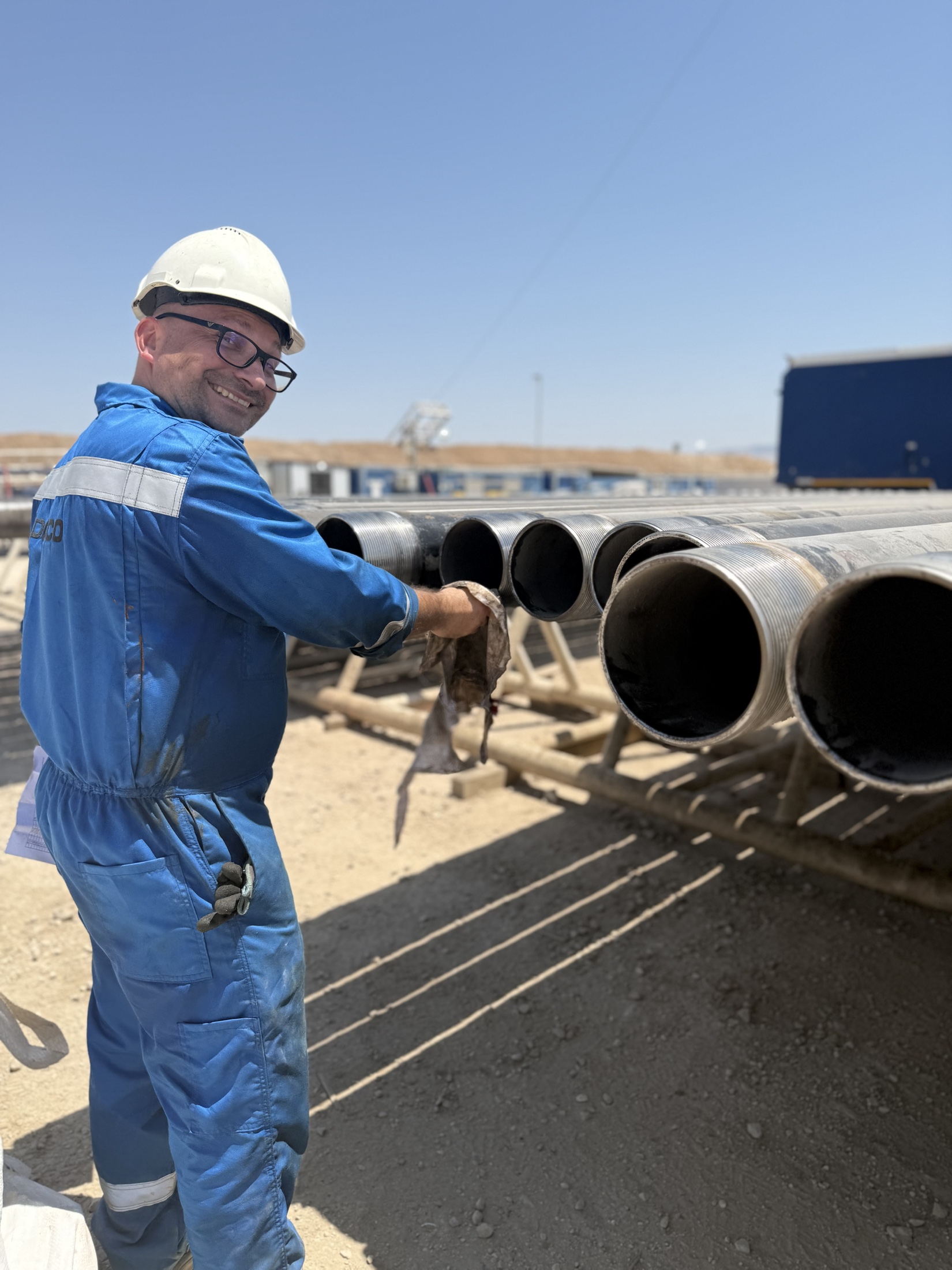 Smiling MJ-02 crew member beside pipe racks
